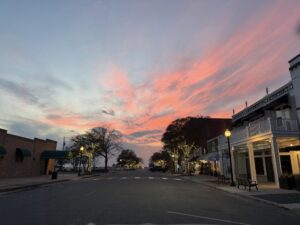 Mason Avenue in Cape Charles, Virginia at sunset with string lights on the trees lining the street and a vivid pink and orange sky overhead