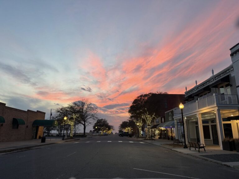 Mason Avenue in Cape Charles, Virginia at sunset with string lights on the trees lining the street and a vivid pink and orange sky overhead