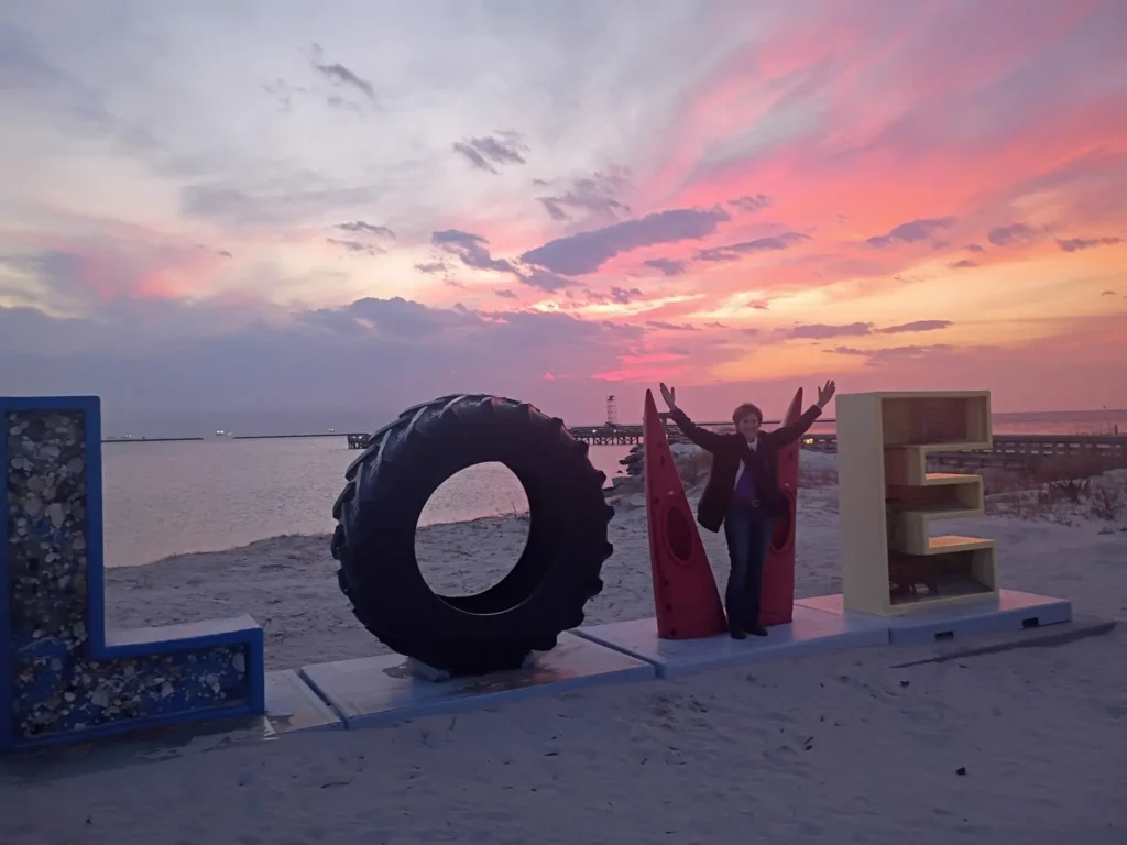 Woman posing at the Cape Charles LOVE sign on the beach at sunset with the Chesapeake Bay and pier in the background