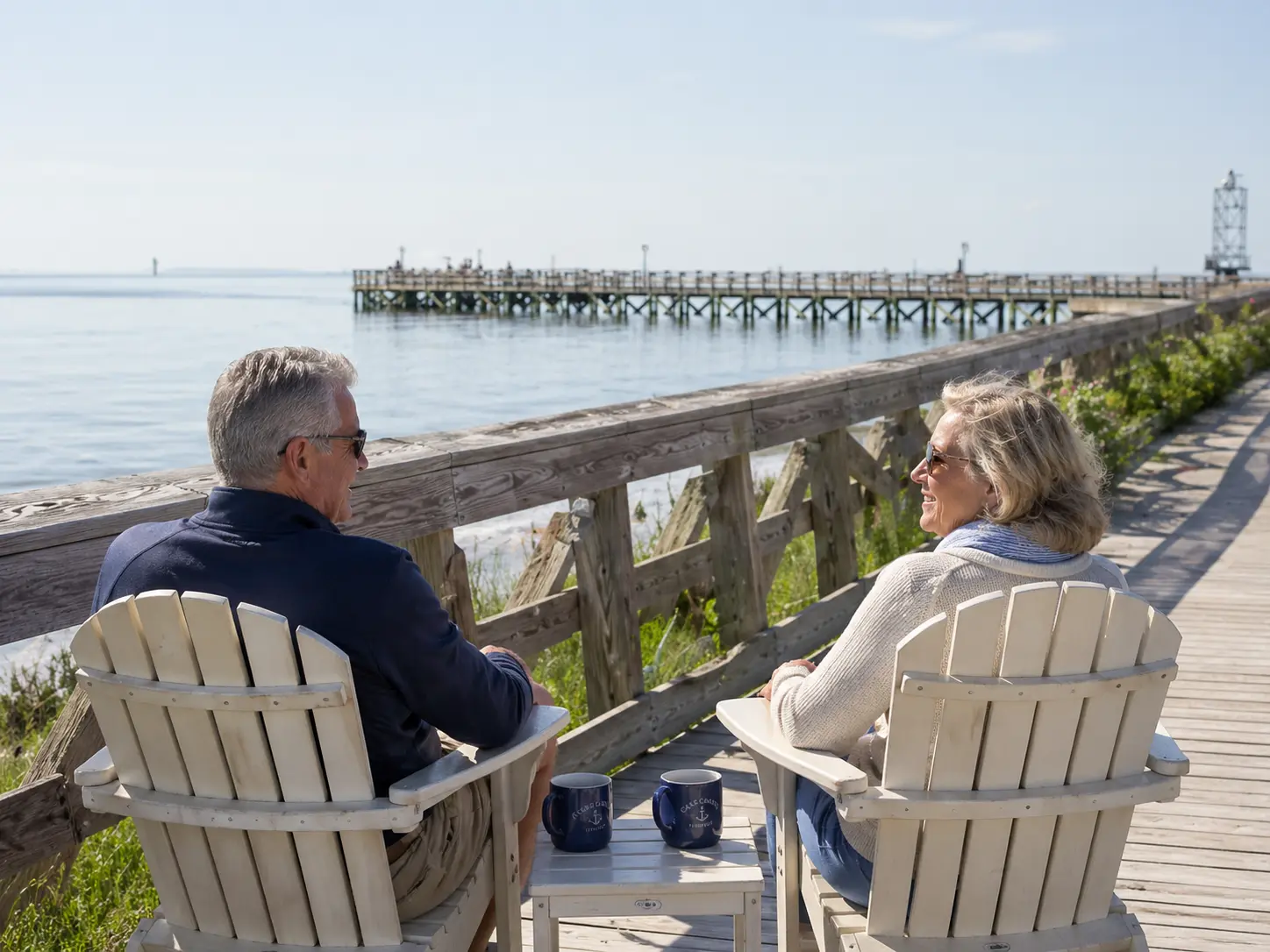 Retired couple sitting in Adirondack chairs on the Cape Charles boardwalk overlooking the Chesapeake Bay and pier