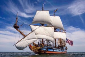 The Kalmar Nyckel tall ship under full sail on the Chesapeake Bay, flying American and Swedish flags against a blue summer sky — coming to Cape Charles for SailFest June 19–21, 2026.