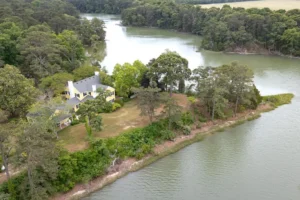 10:21 PM Aerial view of a yellow waterfront home surrounded by mature trees on a wooded peninsula, with tidal creek water on three sides—a classic Eastern Shore of Virginia waterfront property.