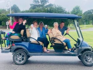 Group of friends riding and waving from a blue six-seater golf cart in Cape Charles, showing why golf carts in Cape Charles are a favorite way to get around